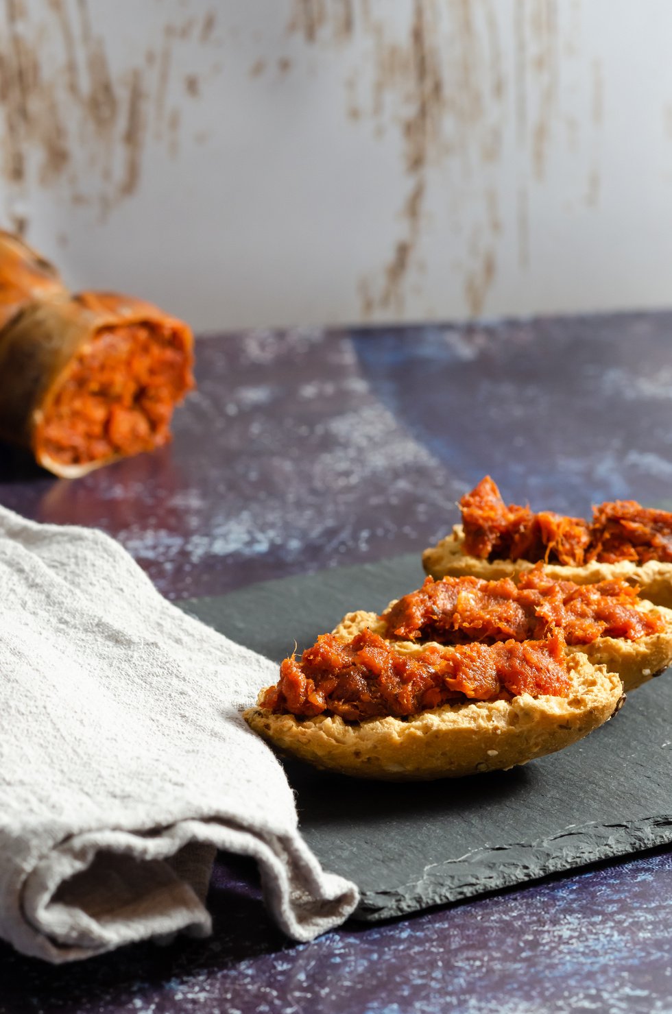 Three sobrasada montaditos on a slate plate with a linen cloth and a sobrasada